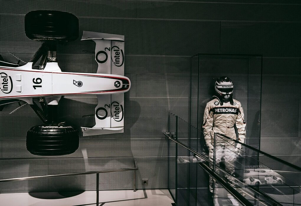 Showcasing a race car and driver suit in a sleek Munich exhibit.