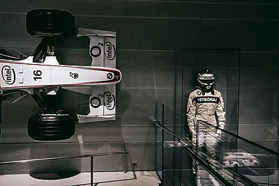 Showcasing a race car and driver suit in a sleek Munich exhibit.