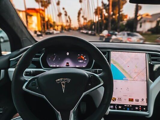 Interior view of a Tesla Model X steering through palm-lined streets of Santa Monica at twilight.