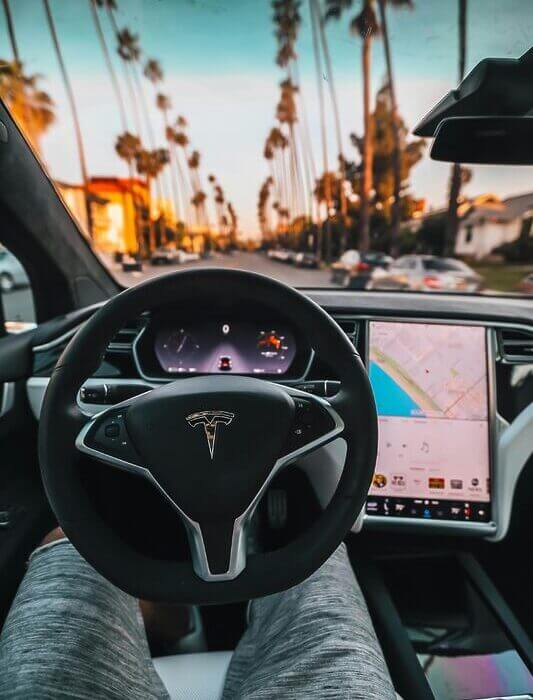 Interior view of a Tesla Model X steering through palm-lined streets of Santa Monica at twilight.