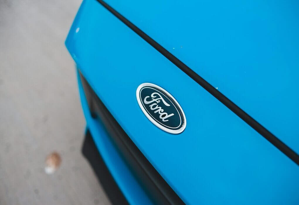 A detailed close-up of a blue Ford car emblem on a sunny day.