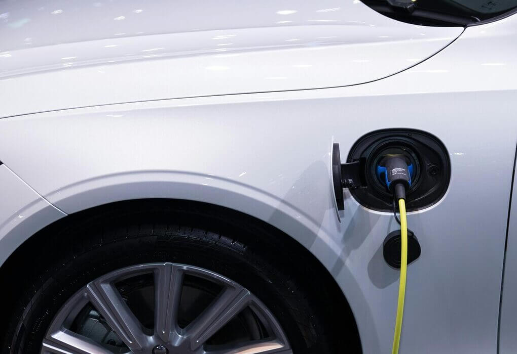 A white electric car is plugged in for charging, close-up view of the charging port.