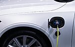 A white electric car is plugged in for charging, close-up view of the charging port.