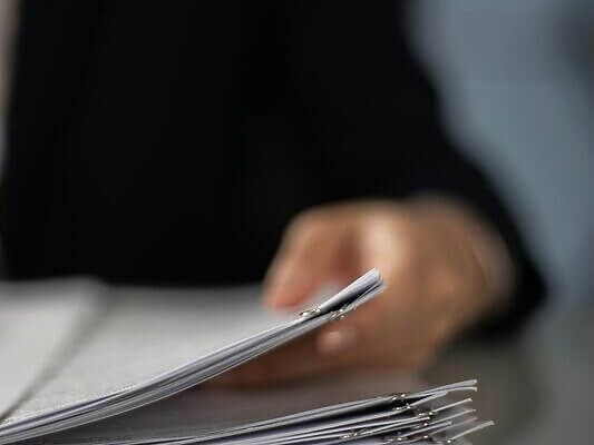Blurred hand holding a stack of documents on a glass desk with focus on papers.