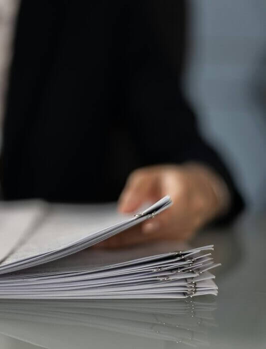 Blurred hand holding a stack of documents on a glass desk with focus on papers.