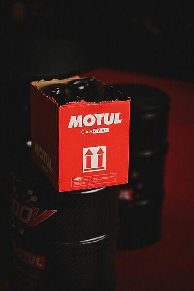 Close-up of Motul car care packaging atop oil barrels in a dark setting.