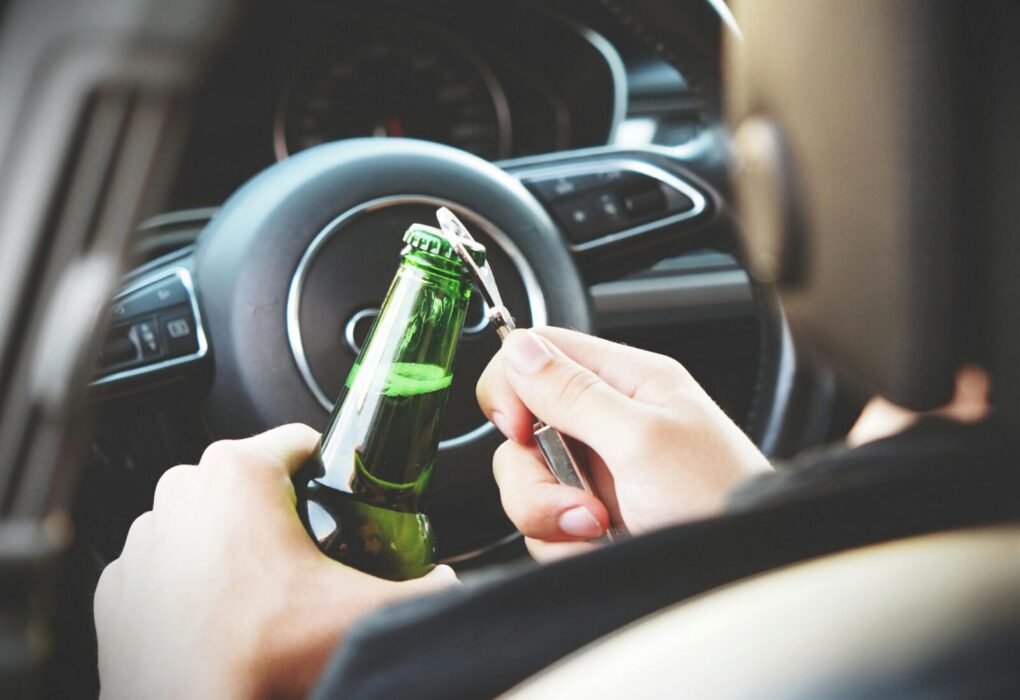 Hands opening a beer bottle inside a car, highlighting the importance of safe driving and awareness of road dangers.