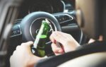 Hands opening a beer bottle inside a car, highlighting the importance of safe driving and awareness of road dangers.