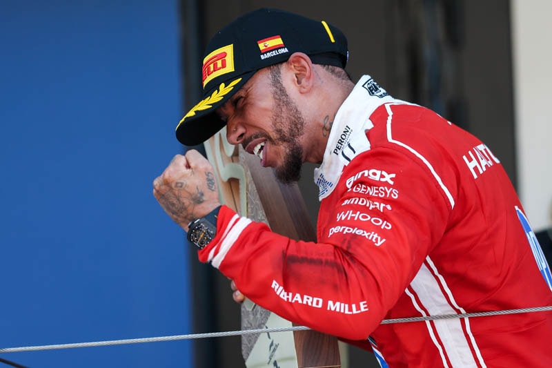 Lewis Hamilton en combinaison Ferrari célébrant sa victoire sur le podium de Barcelone
