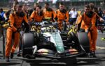Zak Brown dans le paddock de Silverstone avec la monoplace McLaren équipée d’un moteur Mercedes en arrière-plan.