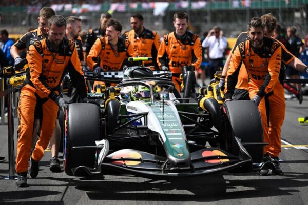 Zak Brown dans le paddock de Silverstone avec la monoplace McLaren équipée d’un moteur Mercedes en arrière-plan.