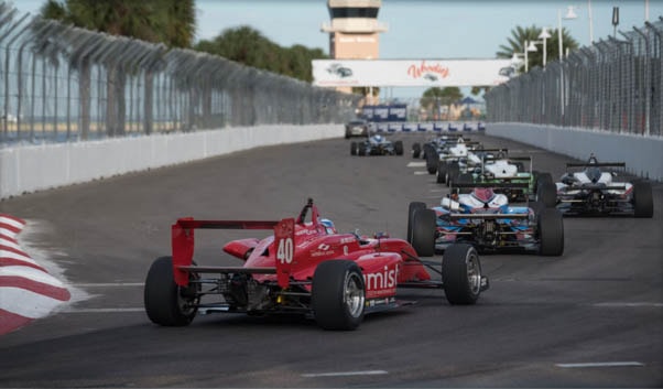 Des spectateurs suivent des monoplaces de Formule 1 depuis une tribune au bord d’un circuit.